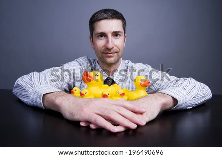 A man with a tie and close-cut hair is holding six rubber ducks.