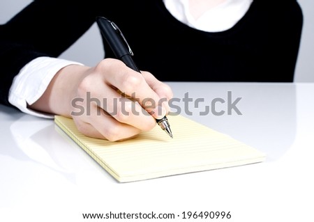 A hand holding a pen over a lined pad of paper.