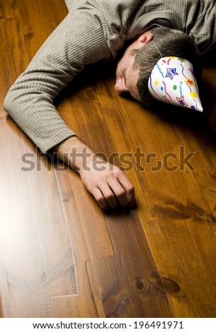 A man wearing a party hat lying face down on a wooden floor.