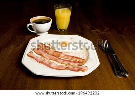 Bacon and eggs on a plate, coffee, and orange juice sitting on a table.