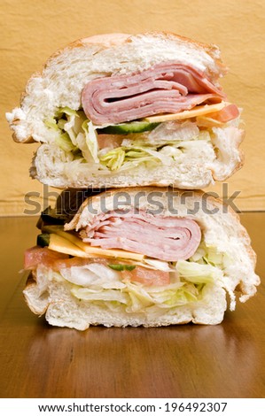A sandwich full of vegetables, cheese and meat sits on top of another sandwich.