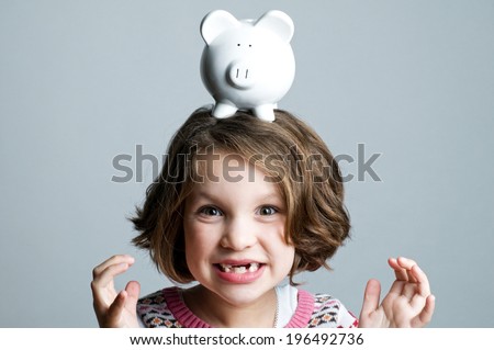 A little girl with missing teeth has a piggy bank on her head.