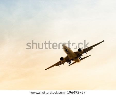 A large airplane at a forty-five degree angle in a pale yellow and blue sky.