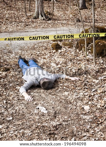 A body lying on the ground in the woods with caution tape strung above.