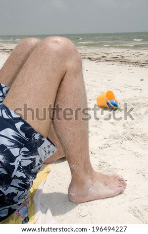 A man wearing blue swim trunks lying on the beach with bent knees.