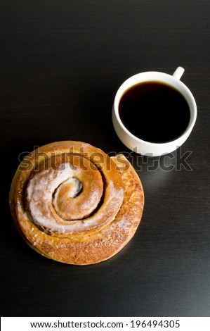 Black coffee in a white mug with a glazed cinnamon bun.