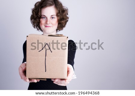 A woman presenting a cube shaped cardboard box marked this side up.