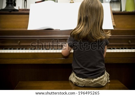 A girl sitting on a stool playing the piano.