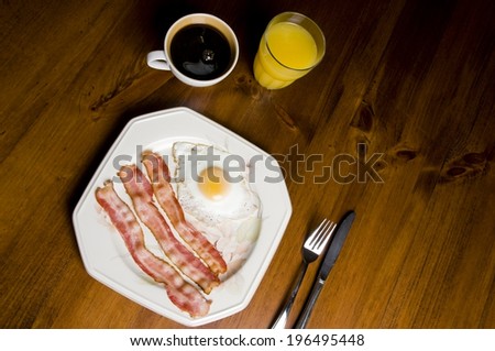Bacon and eggs on a plate, with coffee and orange juice.