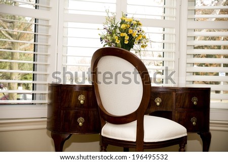 A wooden chair and desk in front of a window with horizontal blinds.