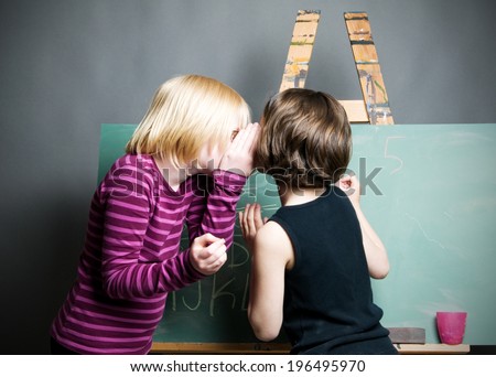 A boy writing the alphabet on the chalkboard while the girl covers her face.
