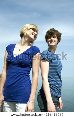 Two women standing back to back, turning to look at each other.
