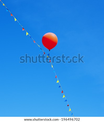 A red balloon and multicolored flags on a string against a clear blue sky.