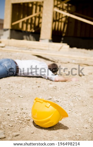 A man lying face down, with his hard hat nearby, at a construction site.