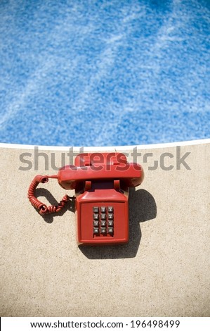 A red corded phone on the edge of a swimming pool.