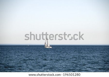 A sailboat alone on the ocean with ripples of waves.