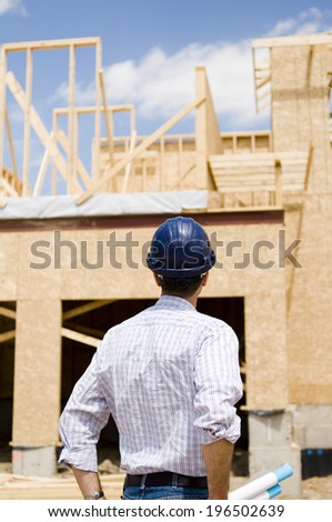 The back of a man in a hard hat looking over a building in progress.