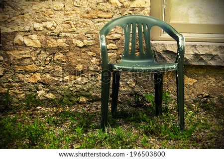 A green plastic chair sitting on grass in front of a stone wall.