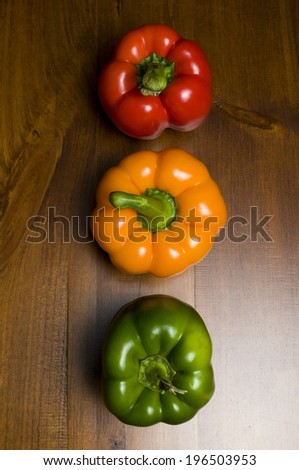 A red pepper, orange pepper, and green pepper sitting in a row on a table.