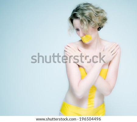 A woman wearing tape around her mouth and private parts with her arms crossed.