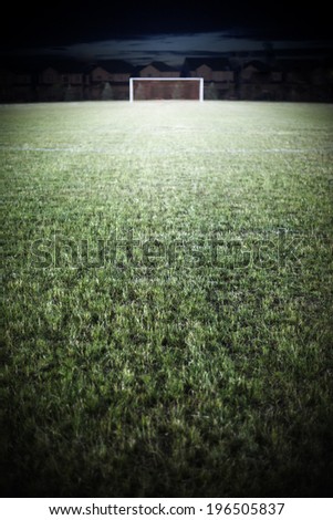 A goal at the other end of a football field at night time.