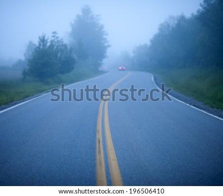 A road on a foggy day with a car ahead in the distance.