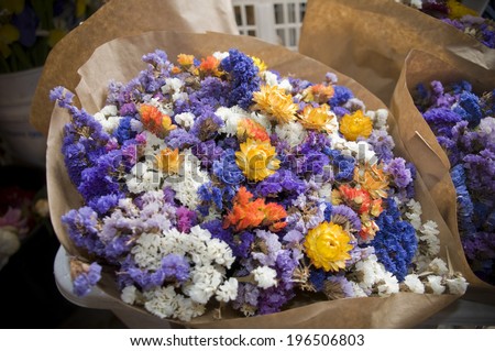 A bouquet of white, purple, yellow and orange flowers wrapped in brown paper.