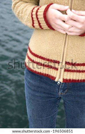 A person wearing jeans and a sweater clutching their hands together in front of their stomach.