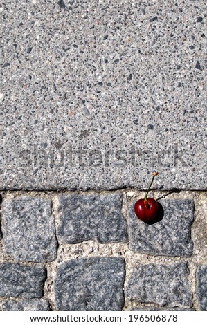 A single cherry on a stone path sidewalk.