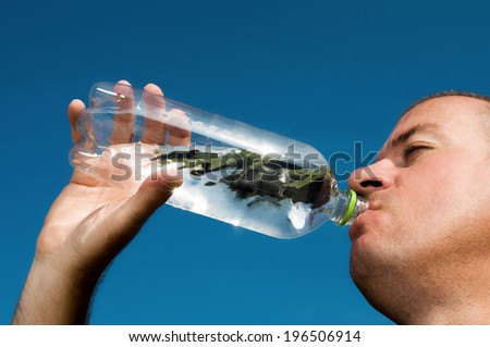 A man drinking from a bottle containing water and a leaf.