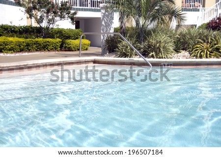 A clean and clear swimming pool with a handle to walk into the pool safely.