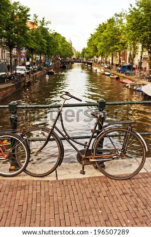 Older bicycle parked on a bridge overlooking a canal in a lively area.