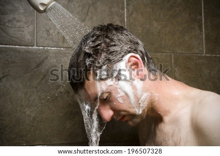 A man with brown hair washing his hair under the shower.