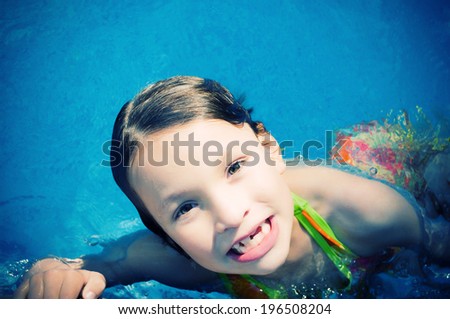 A child with missing teeth swimming in the pool.