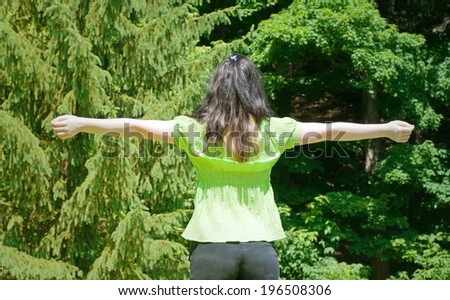A woman standing in front of a group of trees with her arms up.