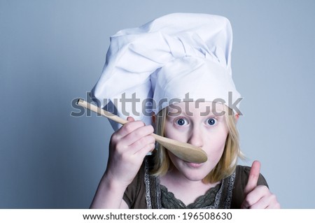 Blonde haired girl giving the thumbs up after licking the wooden spoon.