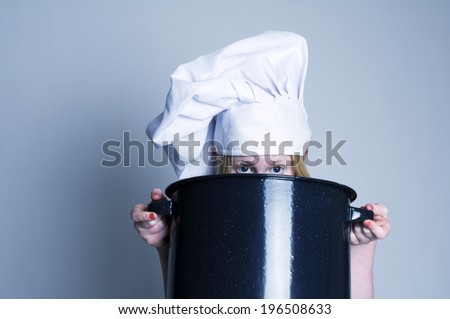 A girl in a chef\'s hat holding a cooking pot.