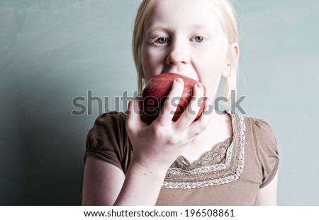 A young girl biting into a large red apple.
