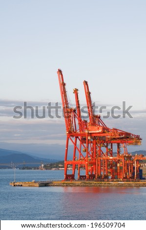 Bright red shipping cranes near a harbor with several containers nearby.