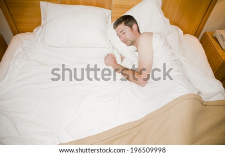 A man sleeping in a bed with white sheets.