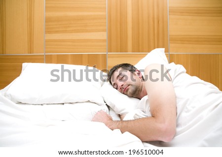 A man sleeps in a bed with a large wooden headboard and white sheets.