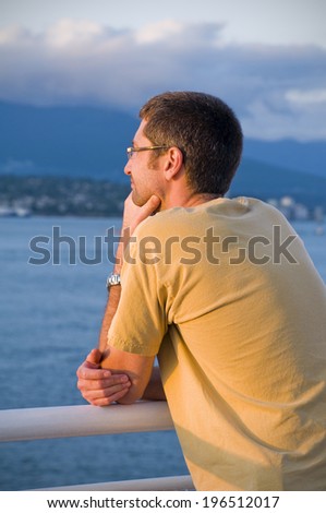 A man in a t-shirt leaning on a rail overlooking water.