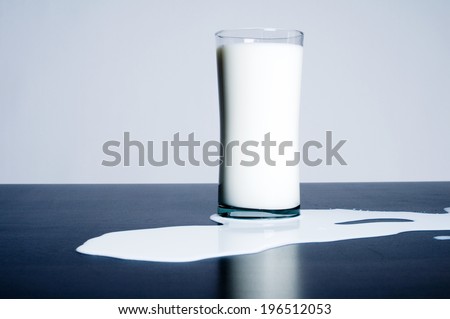 A glass of milk has spilled on a reflective surface.