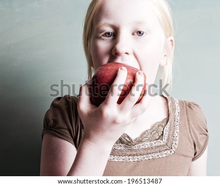 A young, blond girl is biting into a red apple.