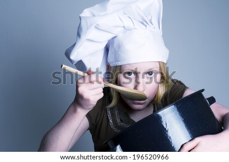 A young child wearing a chef\'s hat tastes from the spoon.