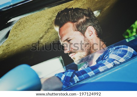 Close-up of a dark haired man driving a blue car.
