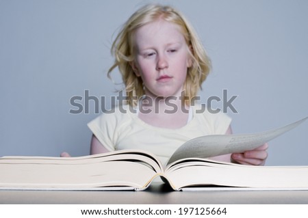 A blond girl turning the page of a book.