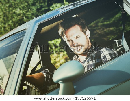 A man looks out his window while driving a blue car.
