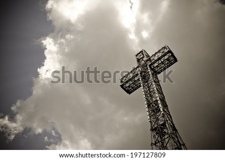 A cross made out of metal beams under a cloudy sky.