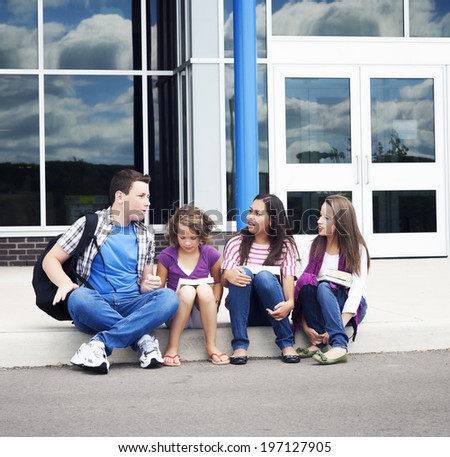 Children sitting on the curb of the sidewalk in front of a building.